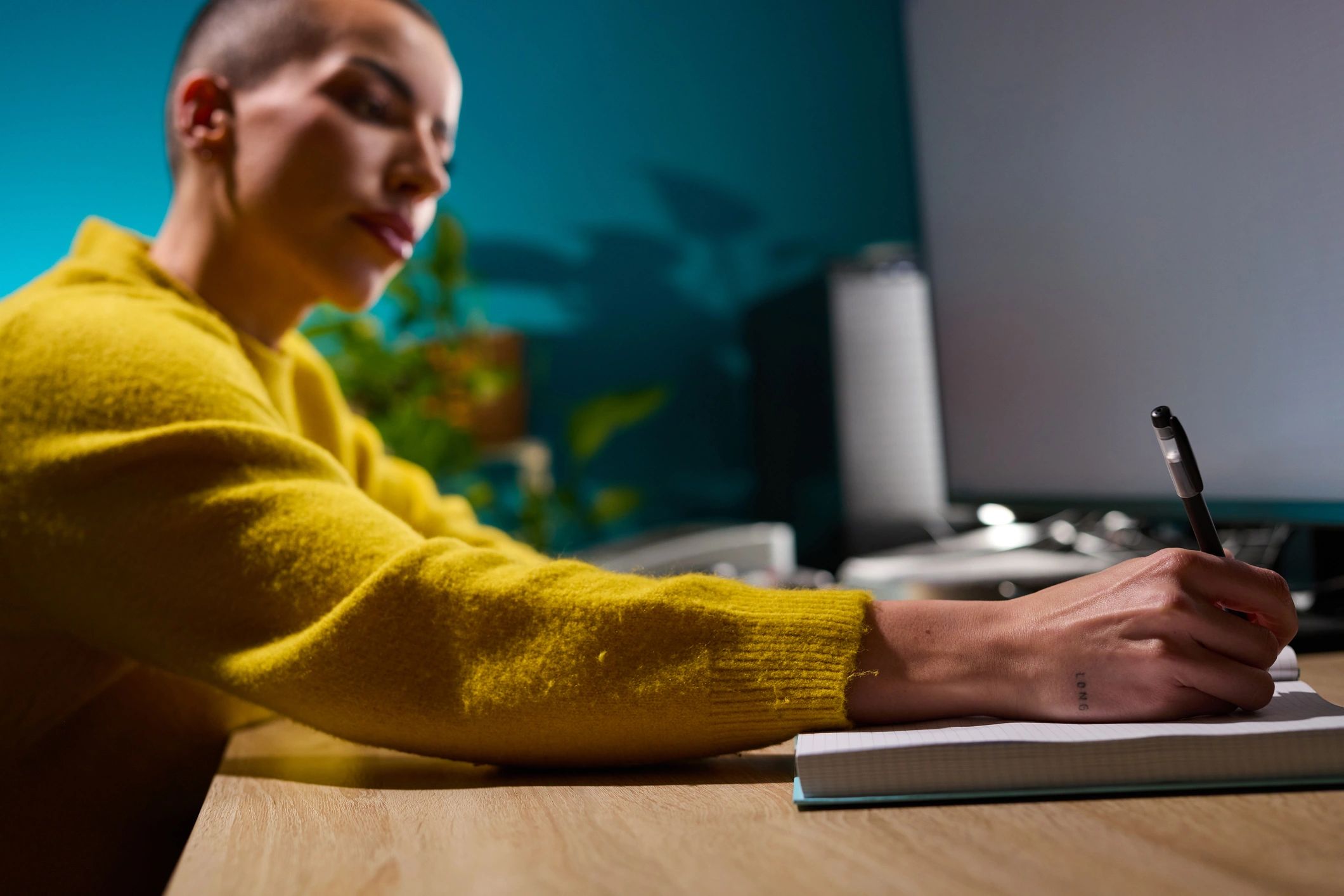 Person writing notes at desk with laptop nearby